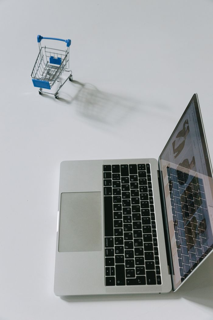 qui-nous-sommes Minimalist scene of a laptop beside a miniature shopping cart symbolizing online shopping.